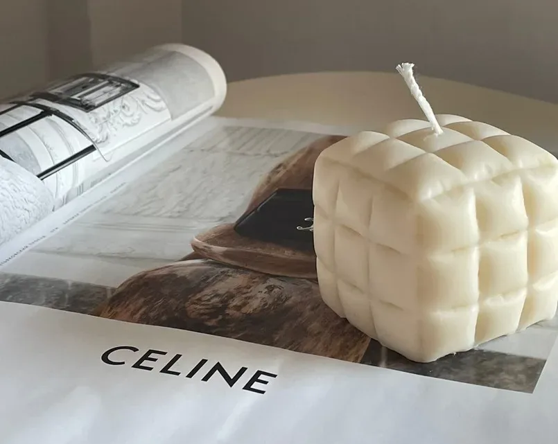 Кремовая кубическая свеча в стиле миним и логотипом CELINE на фоне журнала Кремовая кубическая свеча в стиле миним и логотипом CELINE на фоне журнала