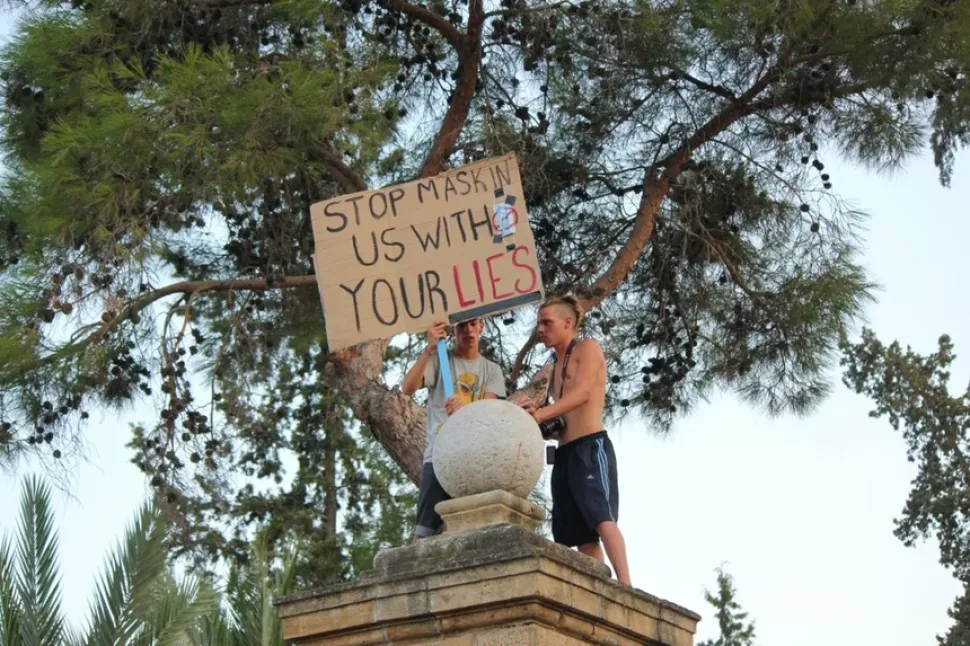 Активист держит плакат «Stop masking us with your lies», поднявшись на колонну ворот