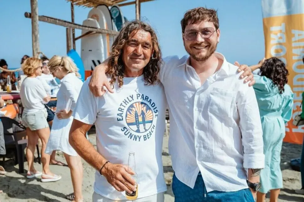 Два человека на пляже Poseidonia среди стоящих SUP-досок и отдыхающих Два человека на пляже Poseidonia среди стоящих SUP-досок и отдыхающих