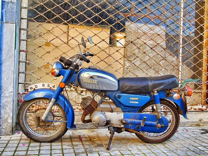 Старый синий мотоцикл Yamaha, выставленный у фасада в Старом городе Лимассол