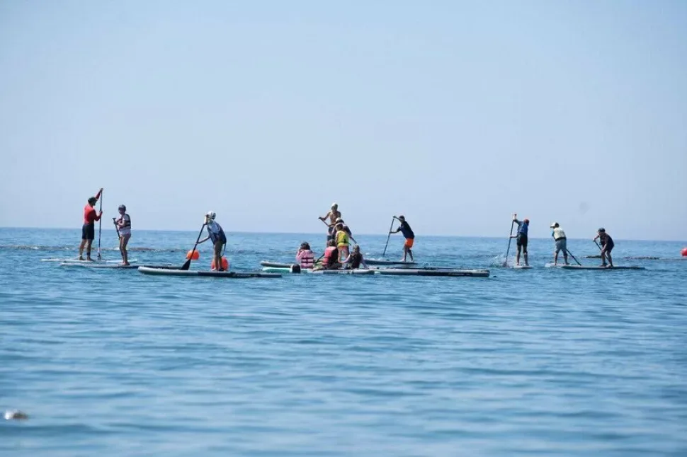 Группа людей на SUP-досках во время коллективного заплыва у побережья Группа людей на SUP-досках во время коллективного заплыва у побережья