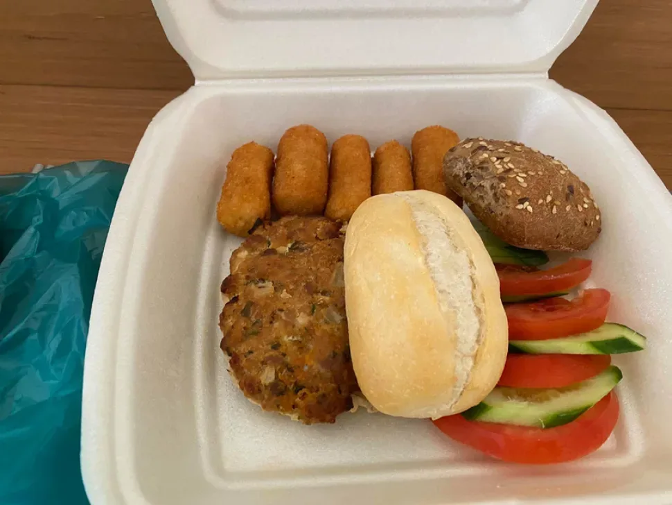 Ланч-бокс с небольшими котлетами, булочками и апельсином на скамейке