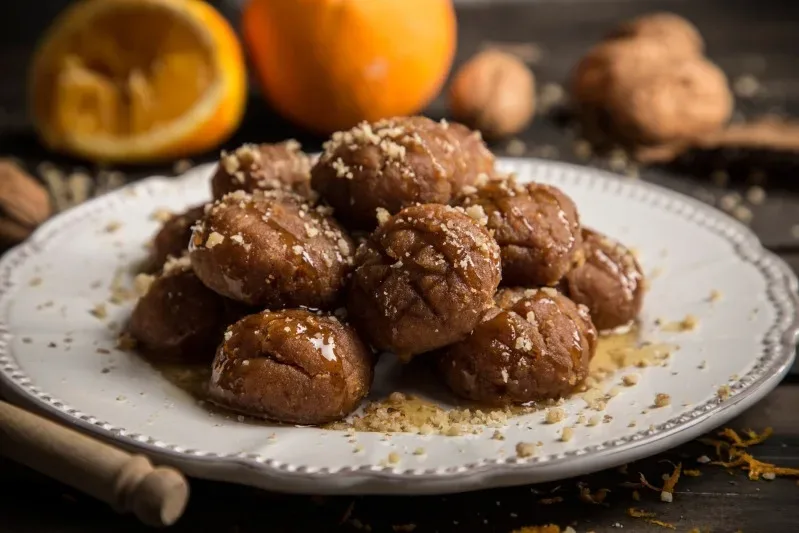 Порция меломакарона, политая мёдом и посыпанная орехами на тёмном фоне