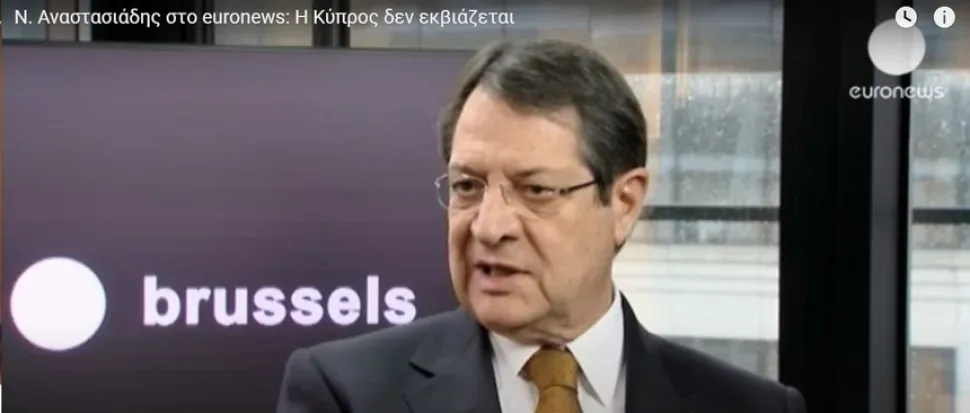 Кадр из интервью: мужчина в студии на фоне надписи brussels и логотипа Кадр из интервью: мужчина в студии на фоне надписи brussels и логотипа