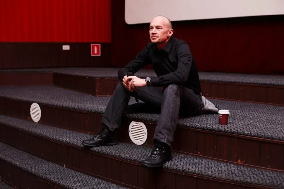 Режиссер в кинозале перед показом «Лето 1989», сидит на ступеньках с кофе