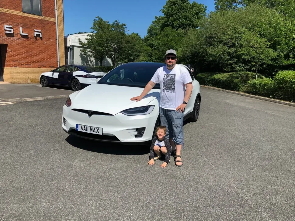 Интервьюируемый с сыном у белого электромобиля Tesla на парковке Интервьюируемый с сыном у белого электромобиля Tesla на парковке