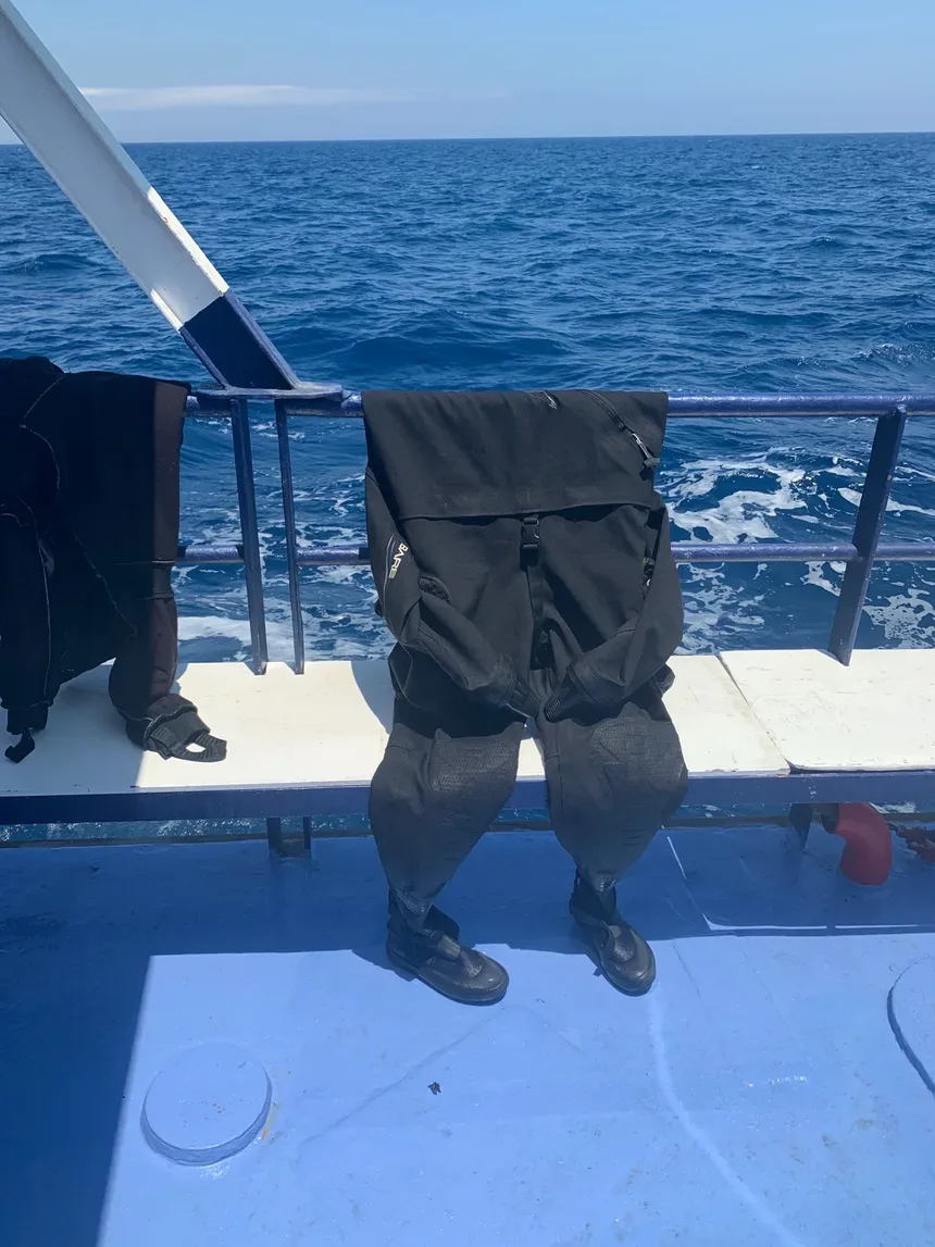 Сухой гидрокостюм и ботинки на поручне лодки в море