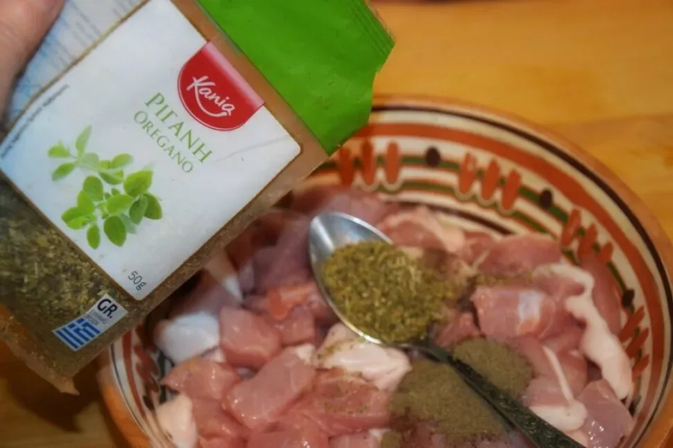 Добавление орегано и специй к кусочкам свинины в миске