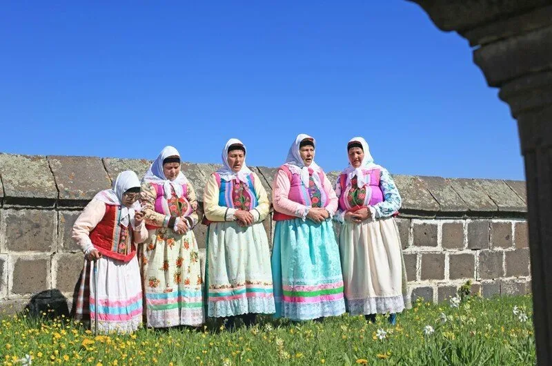 Женщины в традиционных духоборских нарядах у каменной ограды на лугу