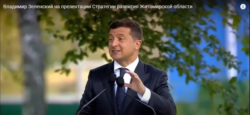 Кадр из видеообращения: мужчина в пиджаке сидит на фоне красного флага Кадр из видеообращения: мужчина в пиджаке сидит на фоне красного флага