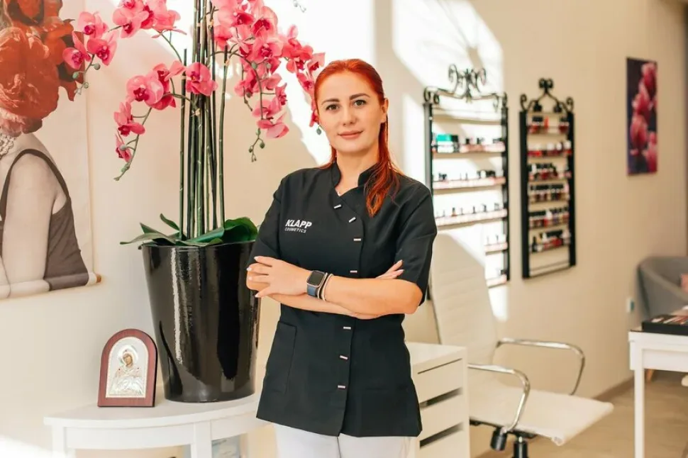 Сотрудница салона L.S. Beauty в рабочей форме на фоне интерьера салона