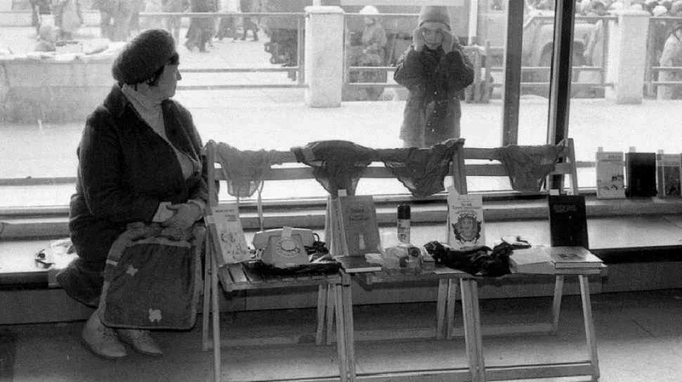 Лавка у витрины с товарами и прохожей на фоне города